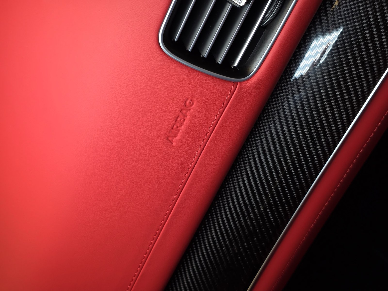 A red leather dashboard with the airbag marking, carbon trim and an air vent